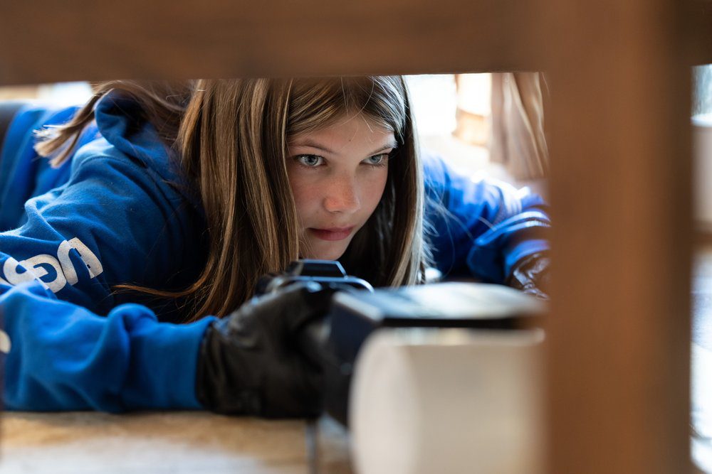Young woman sprays for pests under a cabinet while lying on the floor